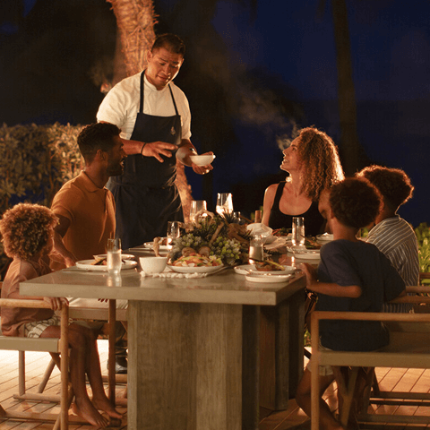 A chef greeting a family as they enjoy dinner outdoors.