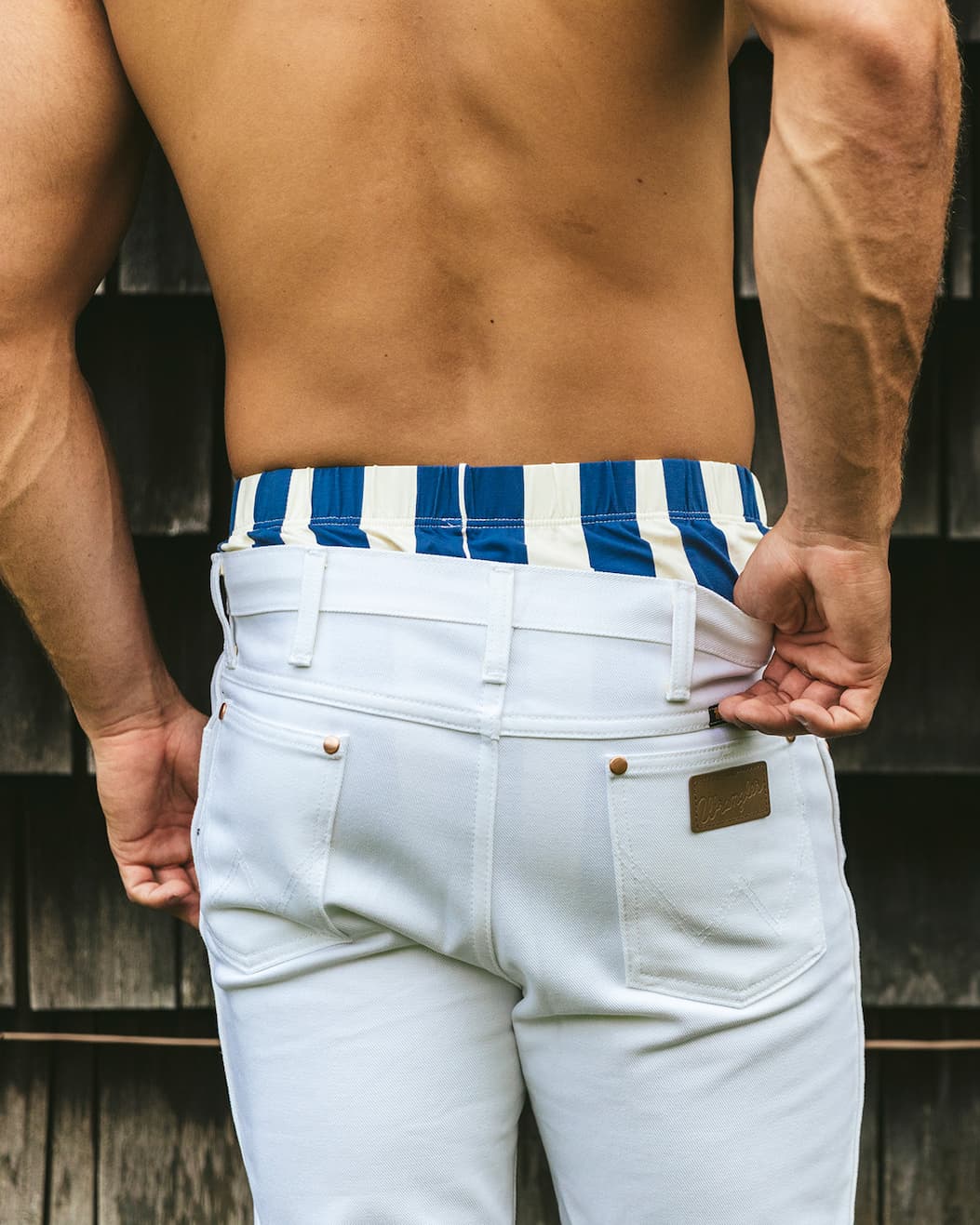 Back shot of shirtless man wearing white pants and blue/cream cabana stripe slim fit boxers