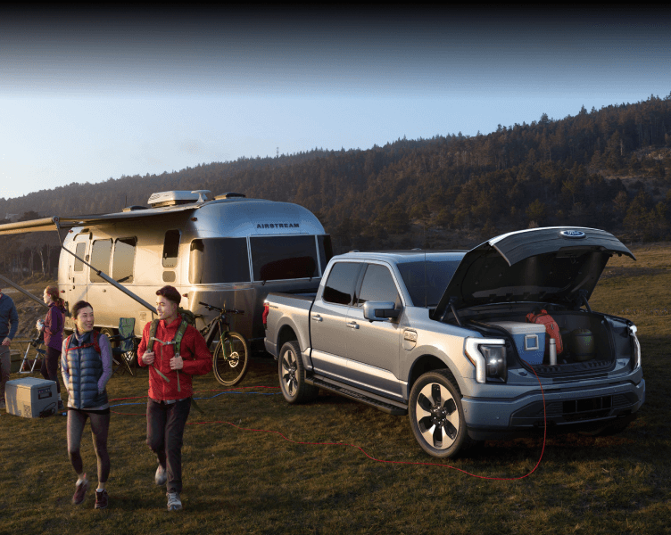 A group of people parked in a field, gray F-150 Lightning and Airstream camper behind them.