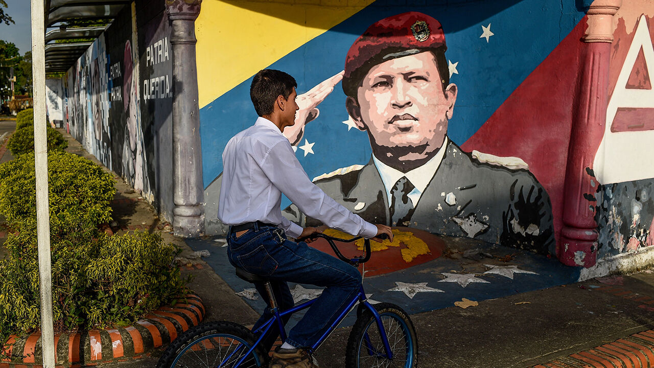 A youngster rides a bike past a mural depicting late Venezuelan President Hugo Chavez.