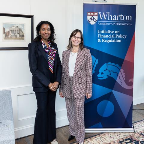 Two people smile for a group photo in front of a banner.