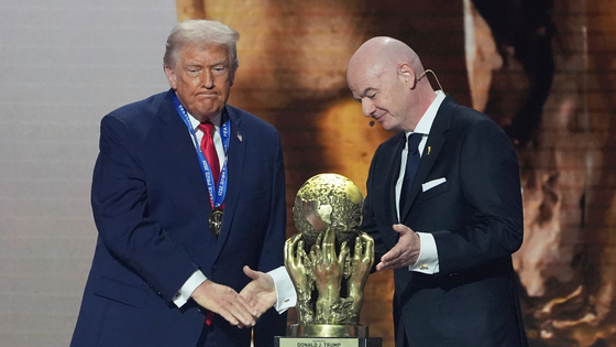 Two men shake hands by a trophy.