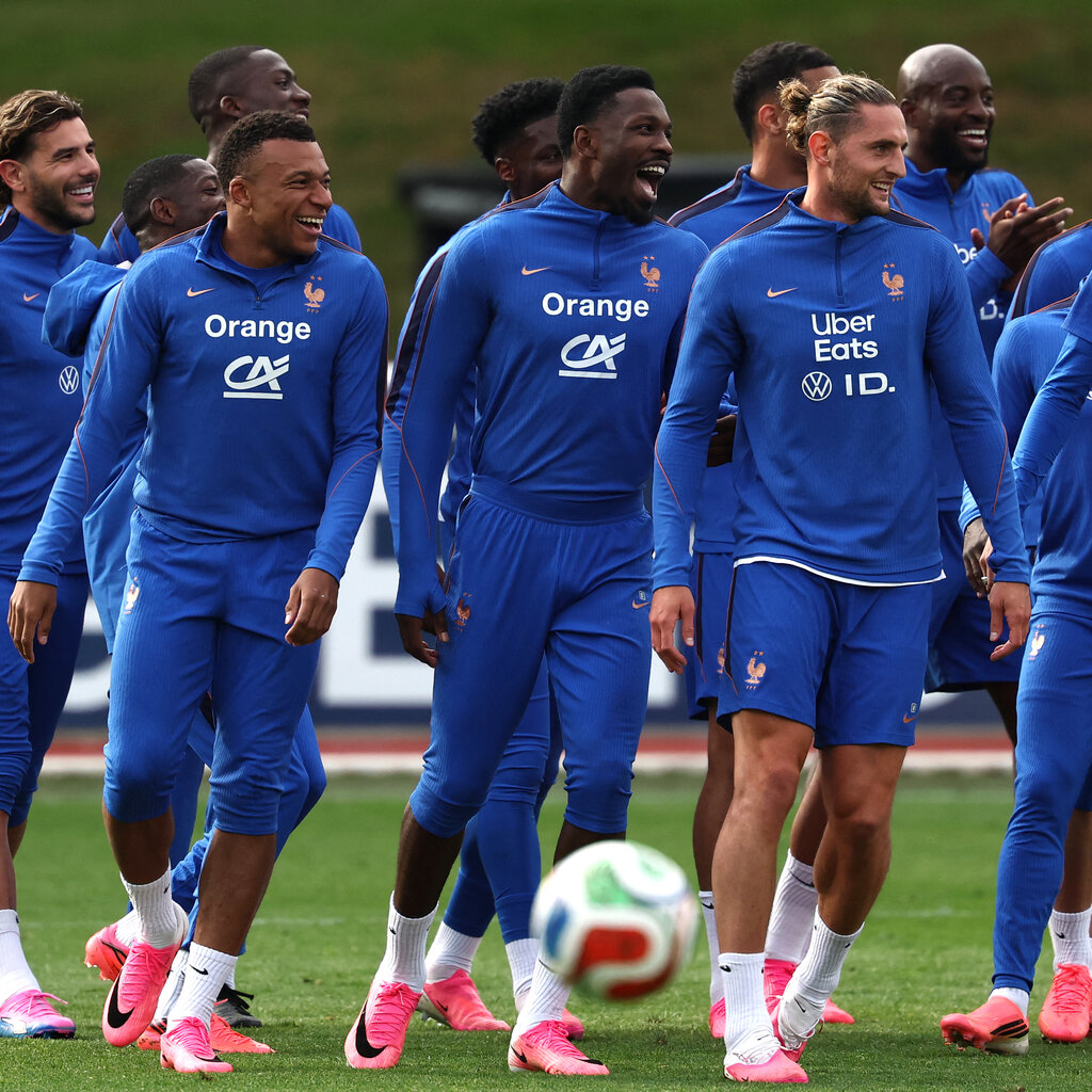 French national soccer team members smile and laugh together on a field while wearing matching blue training uniforms.