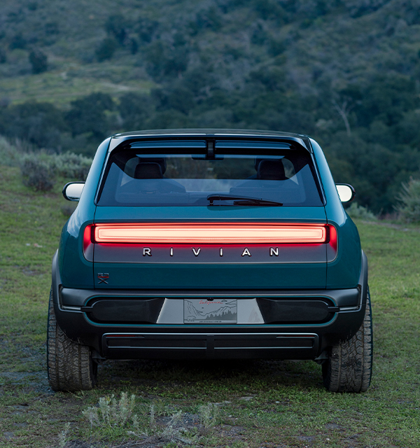 Back of green Rivian car closed boot surronded by green forest