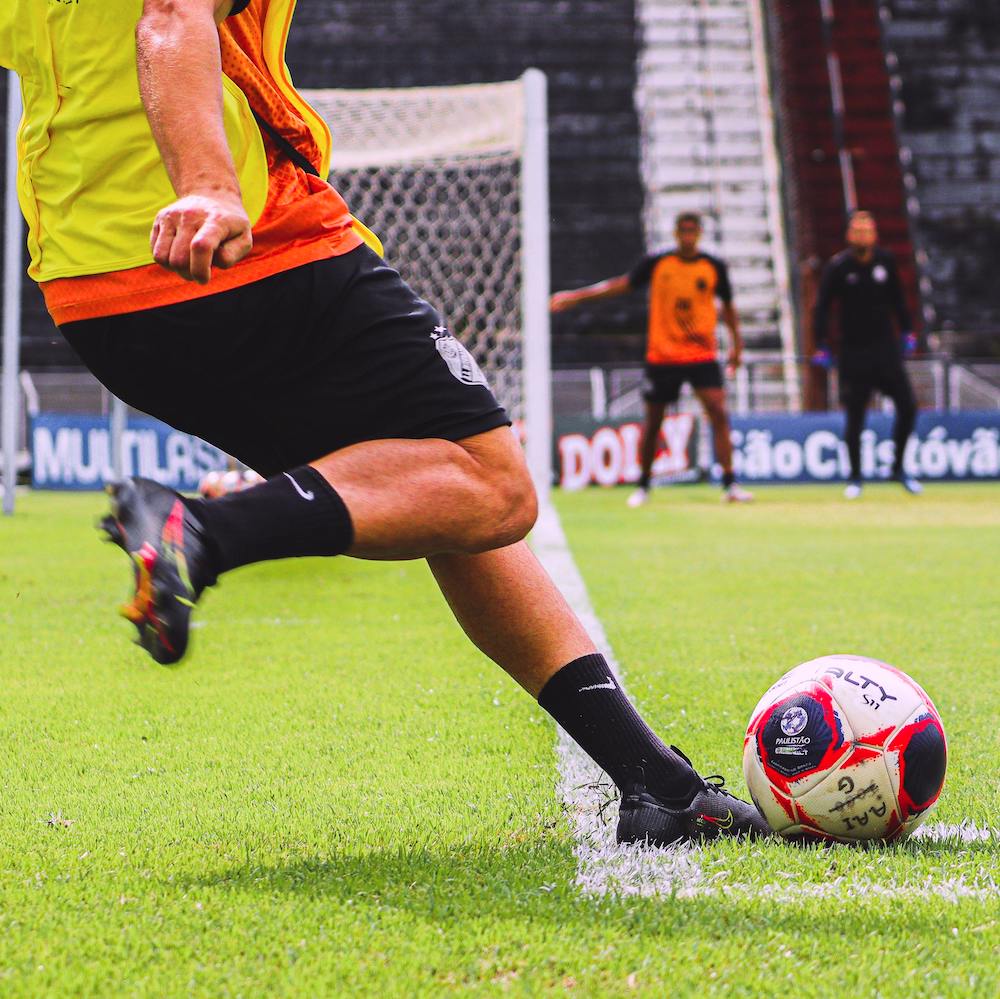A soccer player kicks a ball toward the goal where two other players wait. 