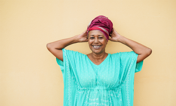 A black woman in a blue dress wears a red head wrap.