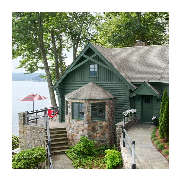 A lakeside home with green painted siding, stone walkways, and a gray roof.