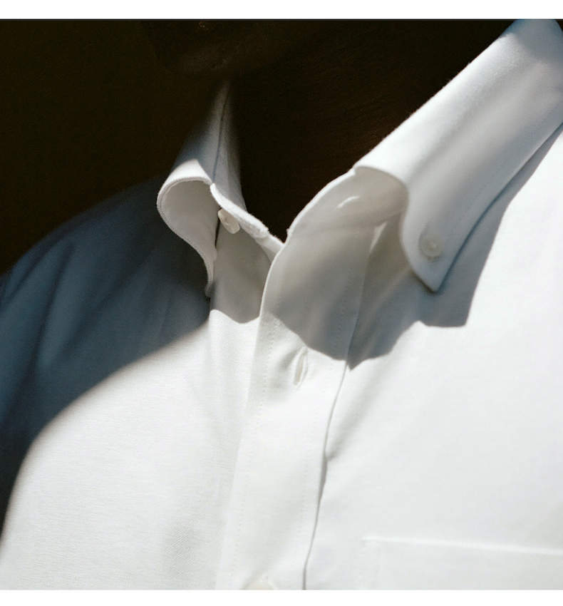 Close-up of the collar and upper chest of a white oxford cloth shirt in sunlight.