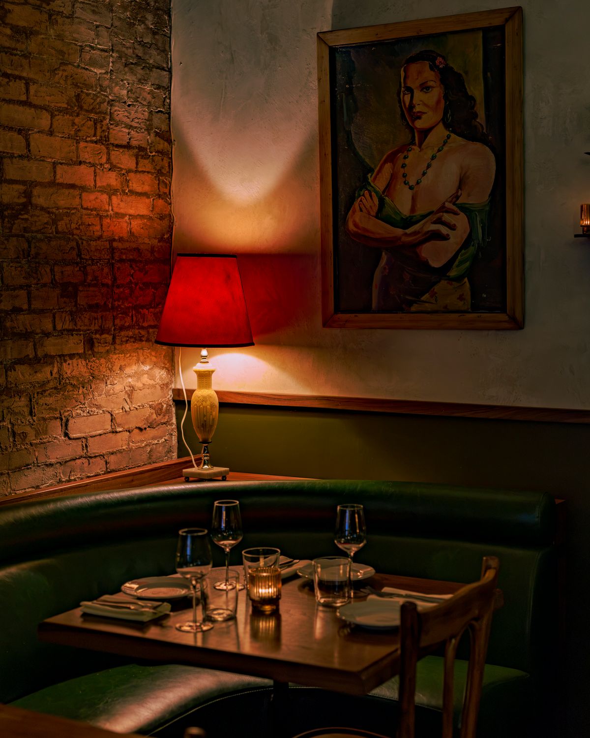 A corner booth seat with a red lamp and a painting above it.
