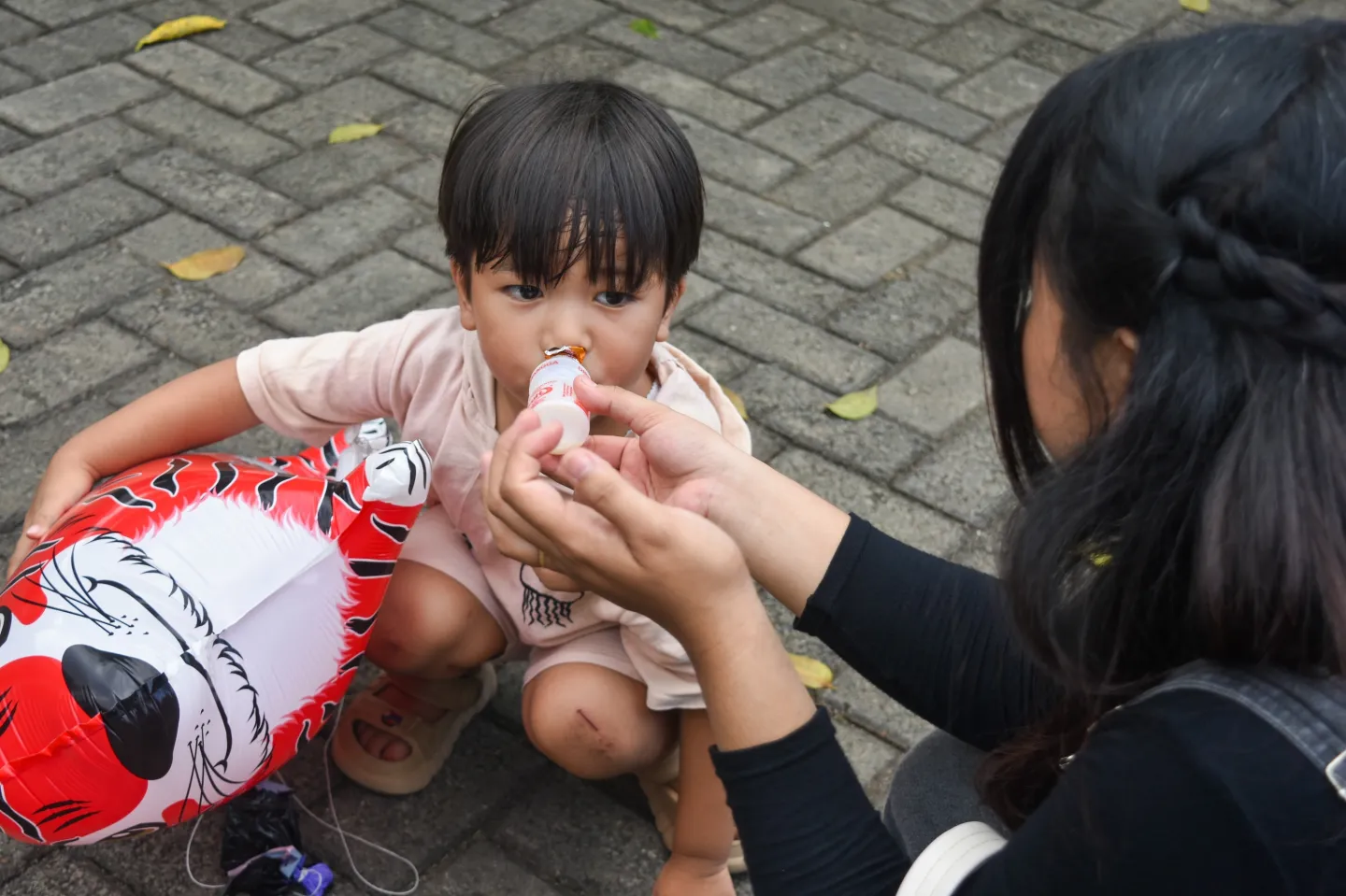 A woman feeding Yakult to a young child