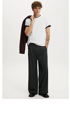 Male model wearing white t-shirt with black cardigan, black pinstriped wide-leg pants, and holding cardigan over shoulder