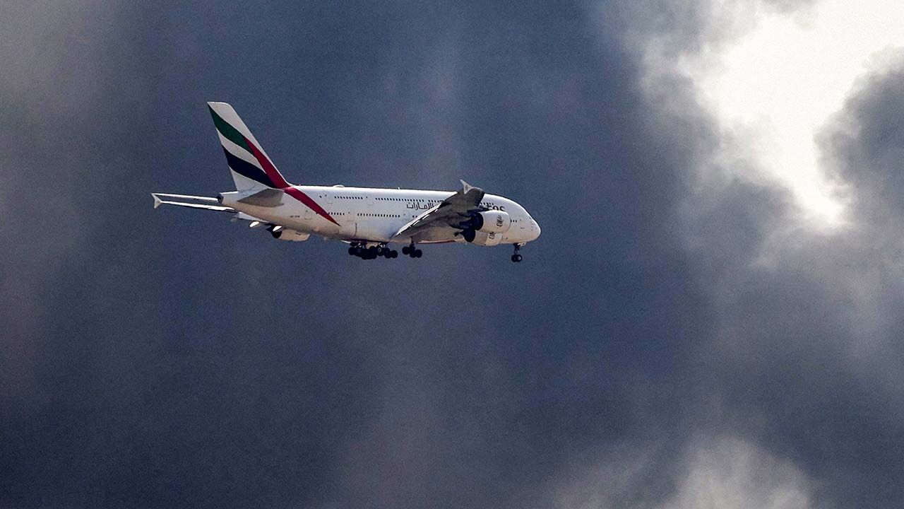 An Emirates Airbus A380 aircraft prepares for landing as a smoke plume rises from an ongoing fire near Dubai International Airport