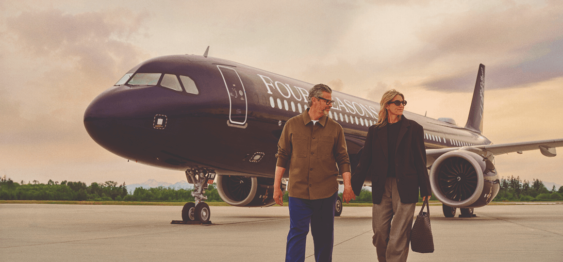 A man and a woman holding hands on a tarmac in front of a jet with Four Seasons written on it.
