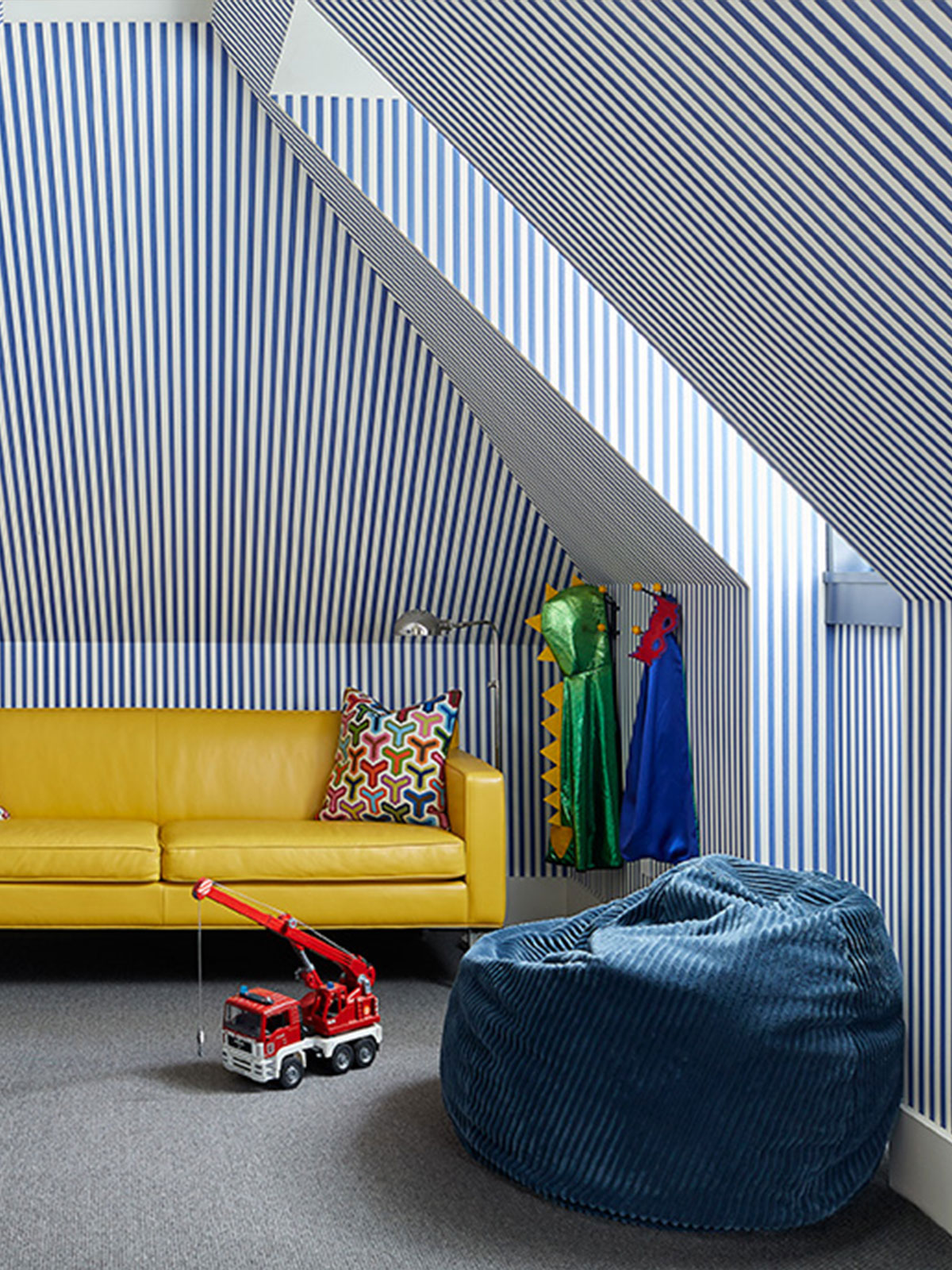 Bold blue-and-white striped wallpaper transforms this attic room into a playful, vibrant space, where bright furniture, graphic patterns and colourful toys combine. The scheme feels imaginative, lively and full of personality.