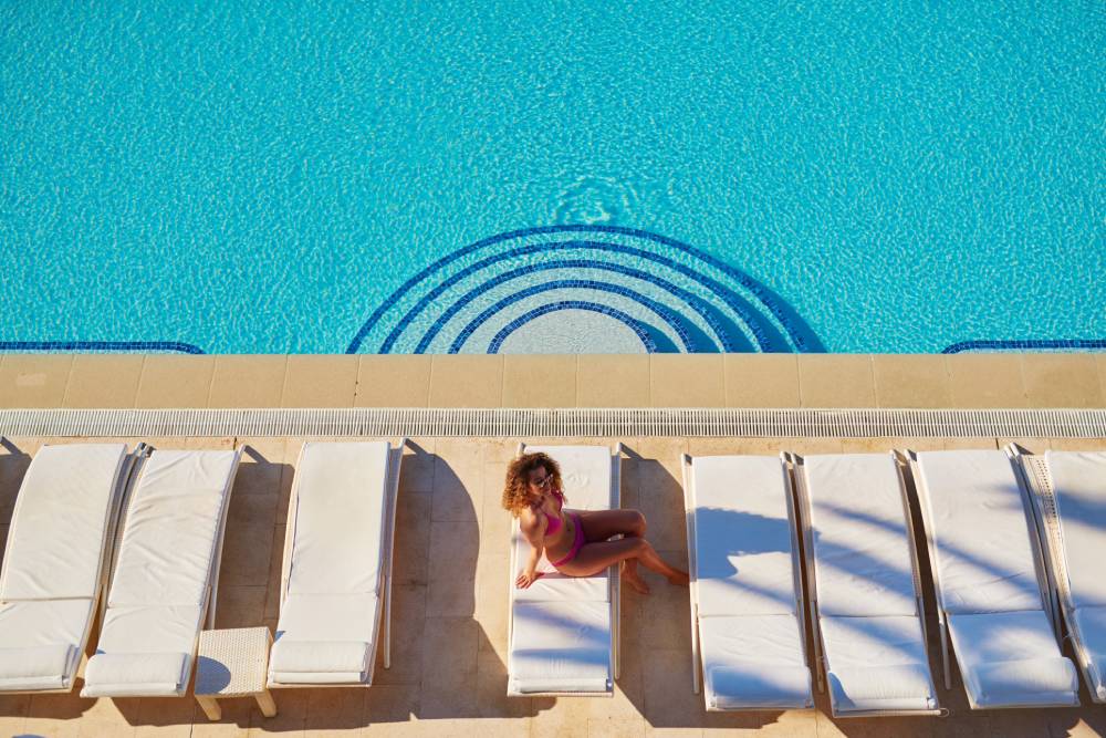 Woman sitting on daybed at pristine pool