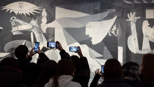 Dark silhouettes of visitors outlined against the illuminated canvas of Guernica from Pablo Ruiz Picasso at Reina Sofia National Art Museum in Madrid, Spain,