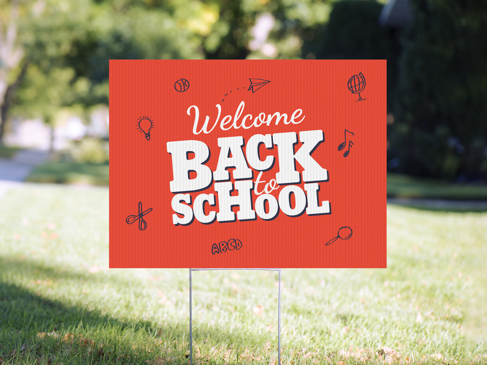 Red back-to-school yard sign with white lettering and school-themed icons displayed on a lawn with metal H-stakes.