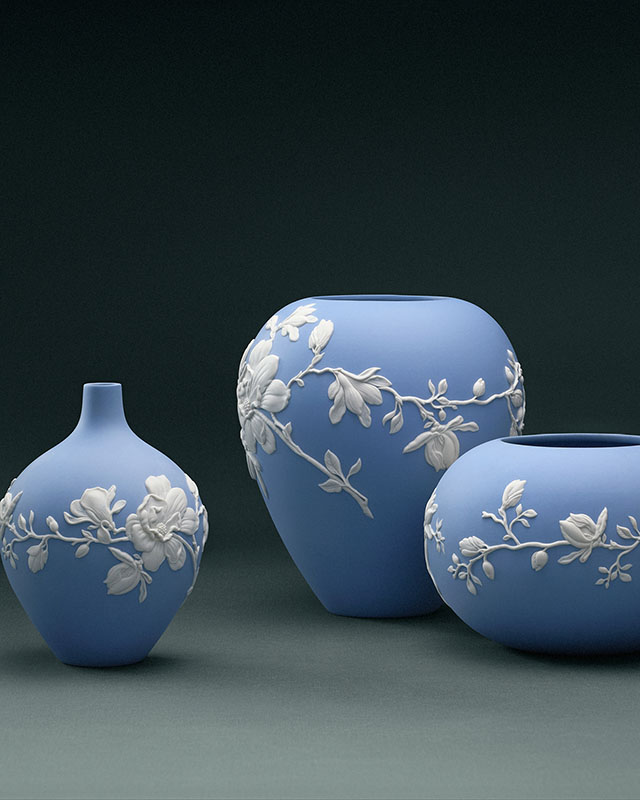 Three blue jasperware vases with white floral motifs sat side-by-side on a plain blue studio background.