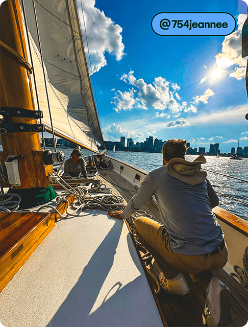 Image description: Two people are sitting on a sailboat, looking at the city skyline on a sunny day.
