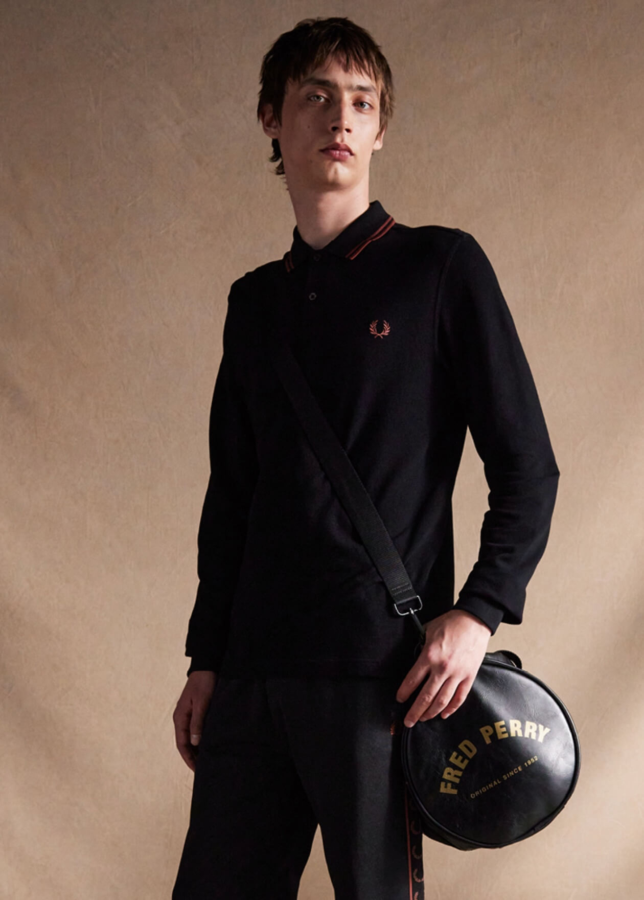 Model wears a Fred Perry Shirt and carries our black barrel bag