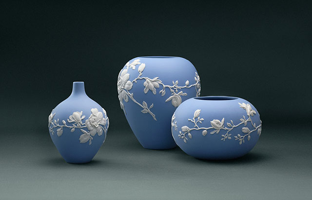 Three blue jasperware vases with white floral motifs sat side-by-side on a plain blue studio background.