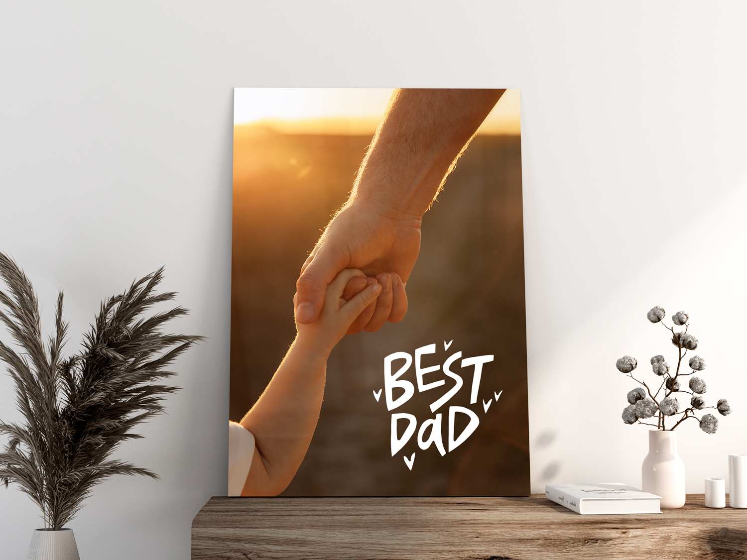 Metal photo print displayed on a wooden console table, showing an adult holding a child’s hand at sunset with “Best Dad” text in white lettering, surrounded by minimalist home decor.