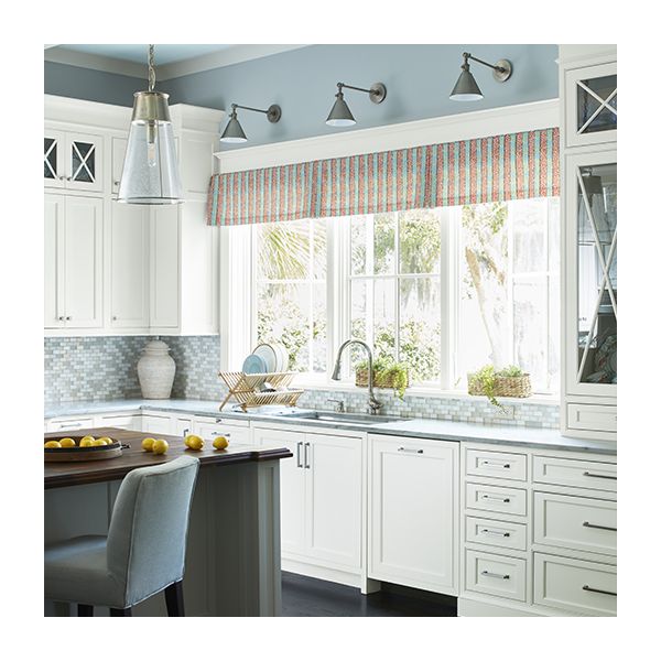 A charming kitchen with white-painted cabinets, light blue upper walls, a pale blue ceiling with white beams, and red striped valance over the windows.