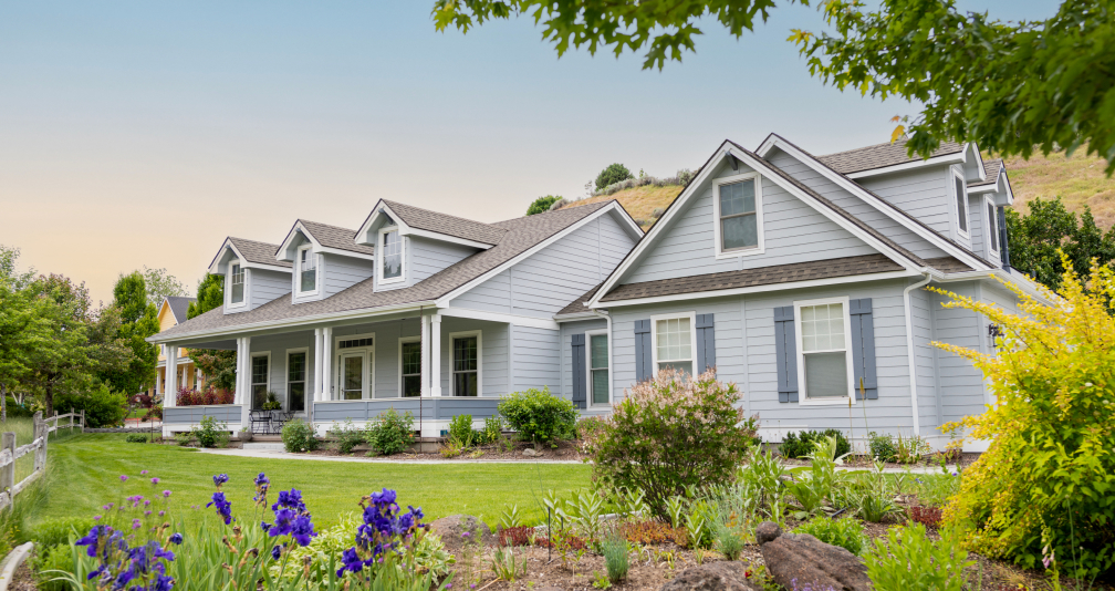 Modern light blue two-story house with a green lawn and blooming flowers.