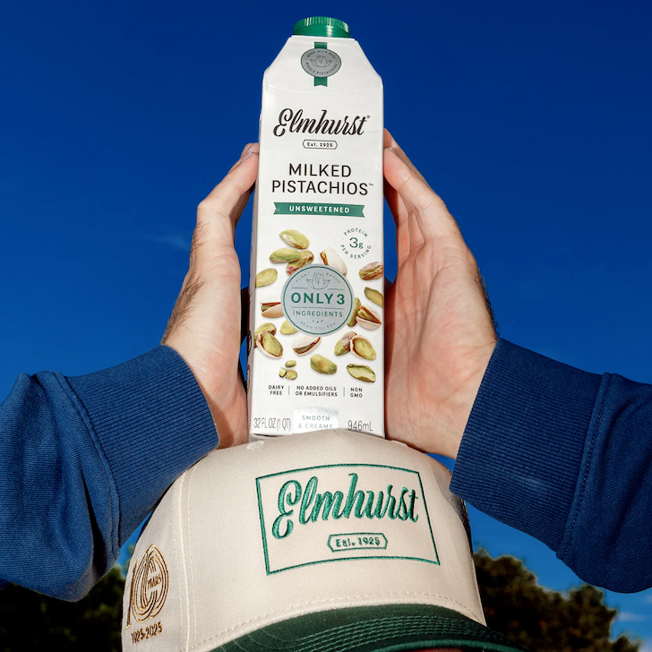 Man holding milked unsweetened pistachios on top of his Elmhurst hat.