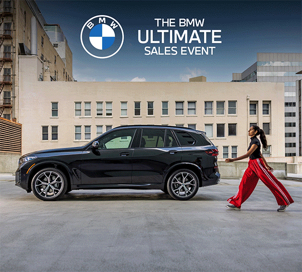 Woman in urban wear walks beside a black BMW parked outdoors.