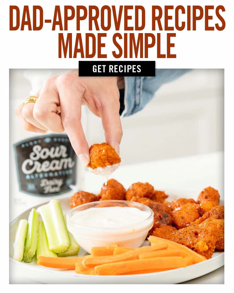 Someone dipping a buffalo cauliflower wing into vegan ranch. Get Recipes.