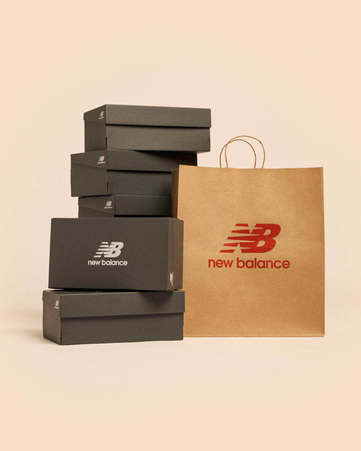A stack of New Balance shoe boxes next to a shopping bag against a pale apricot backdrop