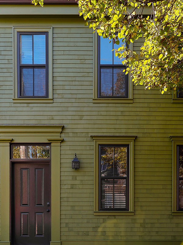 A traditional two‑storey home painted in muted olive green with symmetrical windows and a dark brown front door framed by classic mouldings.