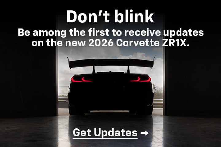 Rear shot of the ZR1X in shadow, tail lights glowing red, as it prepares to exit an open hangar bay door. Don't blink. Be among the first to receive updates on the new 2026 Corvette ZR1X. Get updates.