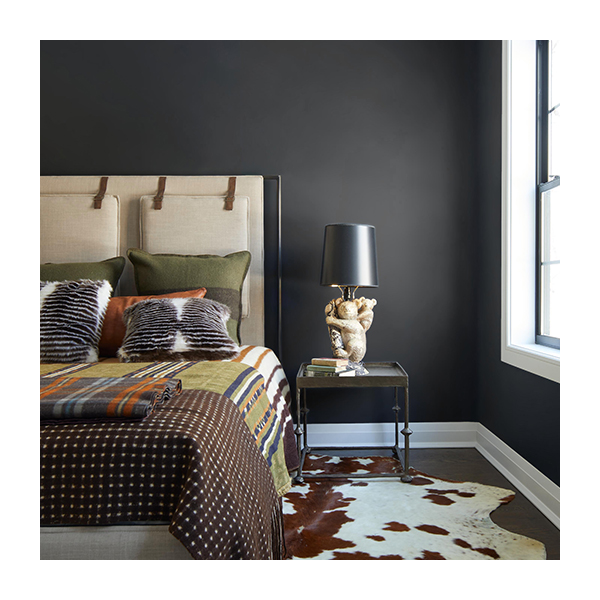Black bedroom walls with a white and brown cow print rug underneath a tan bed with a printed comforter. 