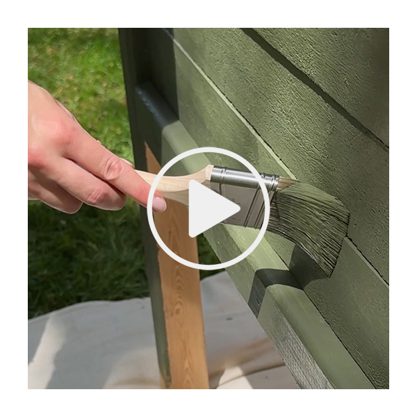 A play button superimposed over a hand holding a paintbrush staining a wooden planter green.