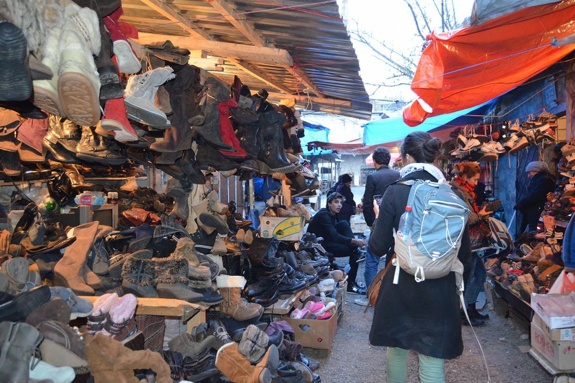 Woman pictured from behind, with a light-blue backpack, walking through a bazaar with stalls of shoes