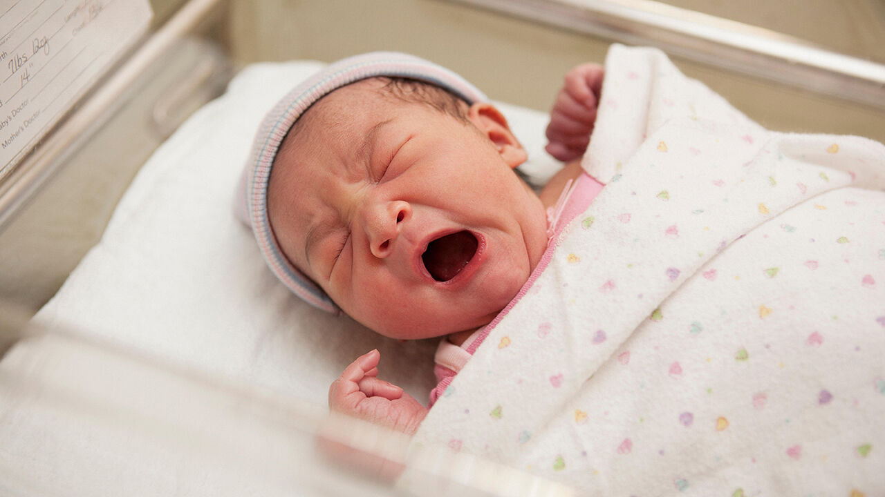 Newborn baby girl yawning in a hospital cot