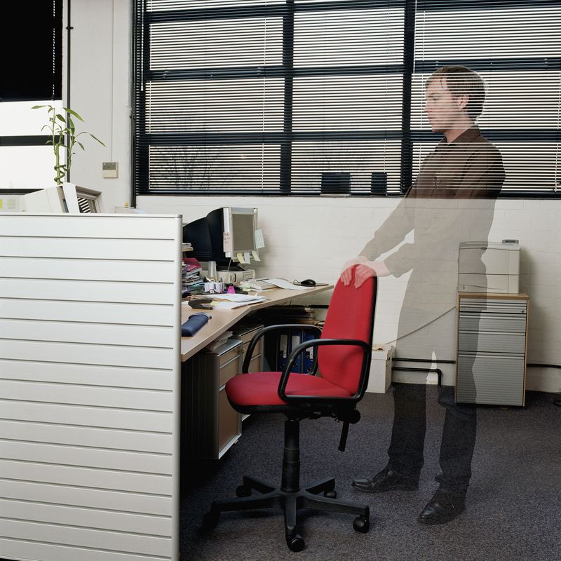 A male ghost standing behind an office chair in a cubicle.