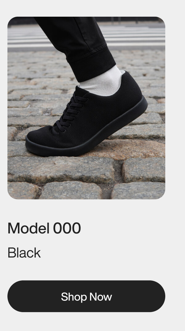 A black sneaker with a sleek design is worn by a person in white pants. The text reads "Model 000 Meteorite." There is a "Shop Now" button below.