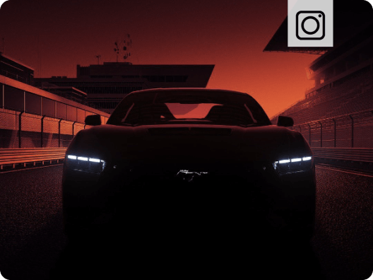 Front‑facing view of a Ford Mustang&reg; vehicle with illuminated headlamps and a dark orange sky in the background