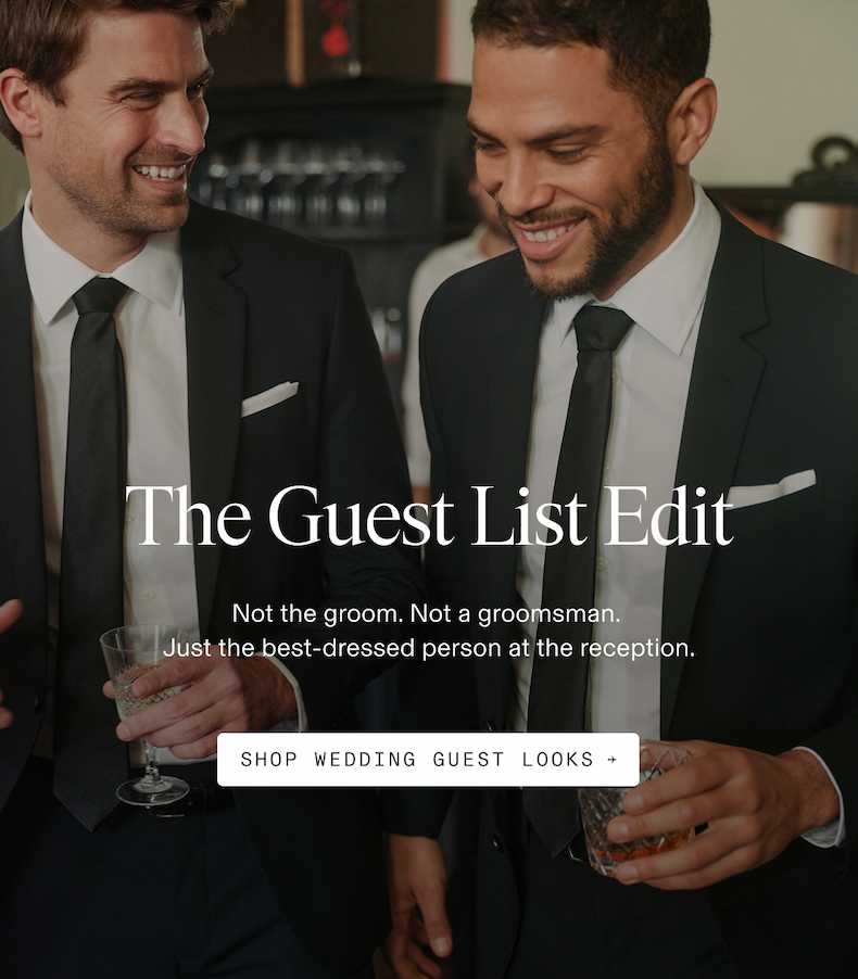 Two men in dark suits and black ties laughing together at a reception bar, holding drinks. The Guest List Edit. Not the groom. Not a groomsman. Just the best-dressed person at the reception. SHOP WEDDING GUEST LOOKS →