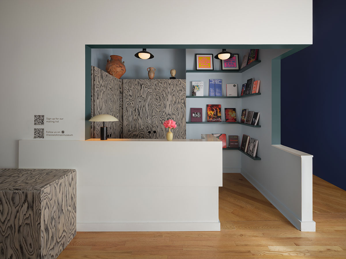 The reception area of the Leslie-Lohman Museum in New York. There’s a white desk built into the space with bookshelves on the wall in the recess behind it. The walls are painted in a light blue with a deeper blue accent on the edges. The colour combination creates a calm feel, like a cool sea breeze.