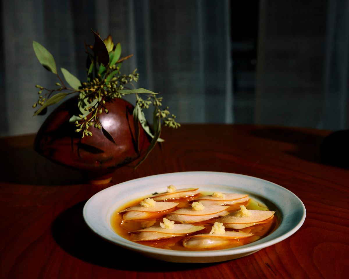 Plate of crudo with pear next to vase with plant