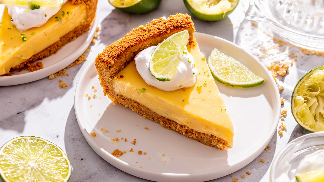 A slice of key lime pie on a plate with freshly sliced lime on top.