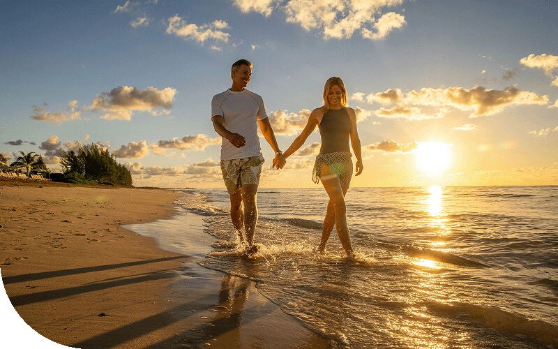 A couple strolls along a Caribbean beach at sunset.