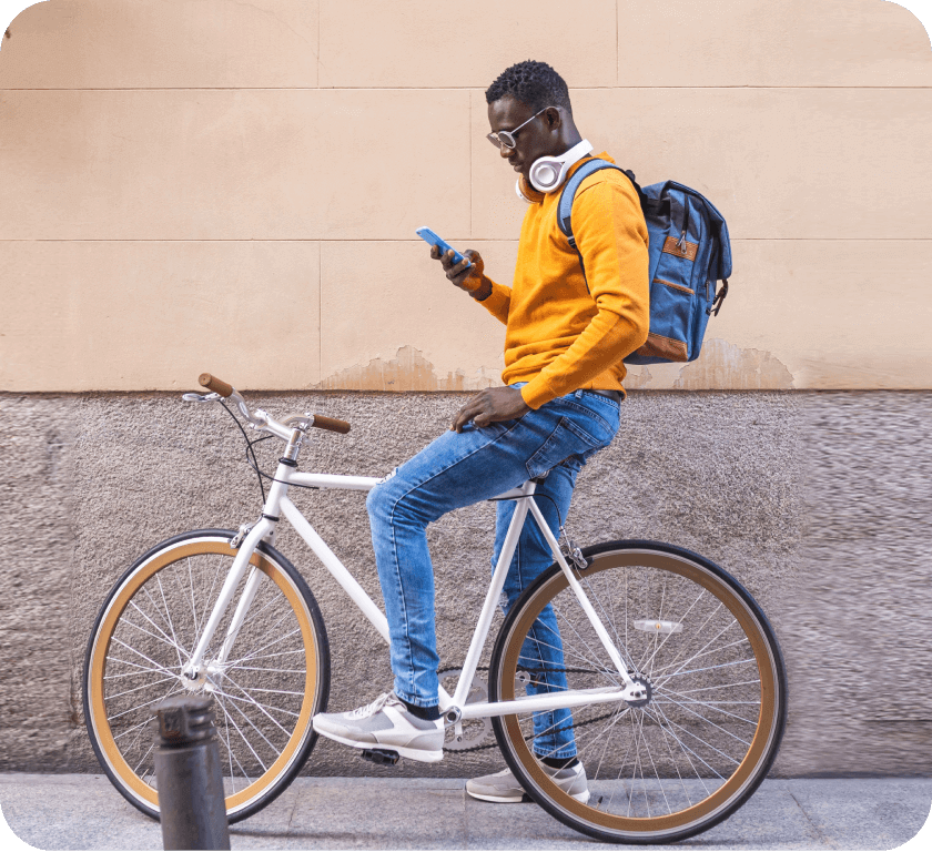 A person with a backpack and headphones on stopped on a bicycle looking at their phone
