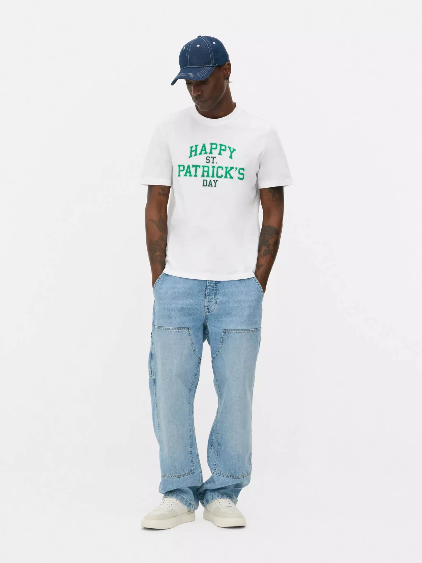 Man wearing a St-Patrick's Day white t-shirt, blue jeans, blue cap and white trainers