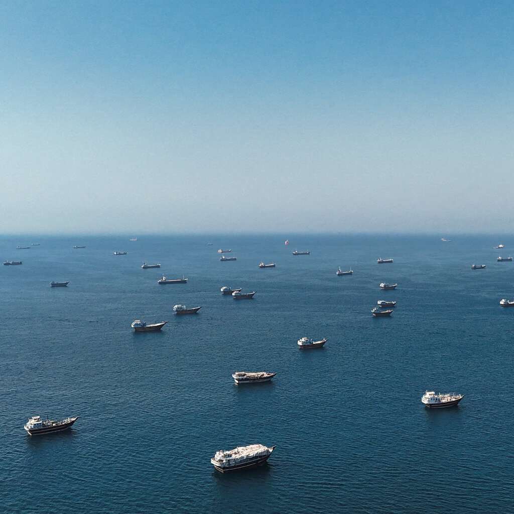 Numerous boats are scattered across a deep blue body of water under a clear blue sky. The horizon line is in the distance.
