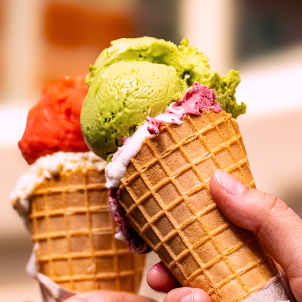 People tap two waffle cones together. One is filled with red ice cream, the other one with green. 